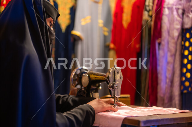 حرف ومهن تقليدية نسائية, تأسيس الدوله السعوديه الاولى ٢٢ فبراير ،يوم التأسيس 1727 م، صورة مقربة من الخلف لخياطة عربية سعودية خليجية ترتدي العباءة السوداء والبرقع تقوم بحياكة وخياطة القماش على الماكينة اليدوية في الأسواق الشعبيه القديمة في السعودية