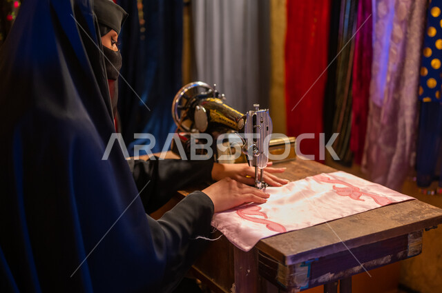يوم التأسيس 1727 م، تأسيس الدوله السعوديه الاولى ٢٢ فبراير ، حرف ومهن تقليدية نسائية، صورة مقربة من الخلف لخياطة عربية سعودية خليجية ترتدي العباءة السوداء والبرقع تقوم بحياكة وخياطة القماش على الماكينة اليدوية في الأسواق الشعبيه القديمة في السعودية