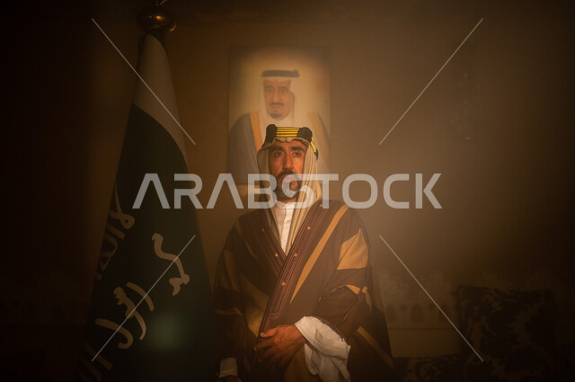 الإسلام  راية التوحيد وشعار الهوية الوطنية, مفهوم الفخر والاعتزاز وحب الوطن، يوم بدينا 1727 م، صورة مقربة لرجل عربي سعودي خليجي يرتدي الشماغ والثوب التقليدي يقف جانب علم المملكة ينظر إلى الكاميرا، ذكرى تأسيس الدولة السعودية الأولى 22 فبراير
