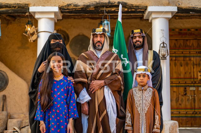 Anniversary of the founding of the first Saudi state, February 22, a Saudi Gulf Arab family wearing popular costumes on holidays and national occasions, standing in one of the heritage houses built of mud, looking at the camera with gestures of pride, pride and happiness, Day of Dina 1727 AD.
