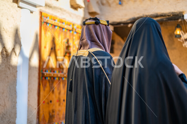 يوم بدينا 1727 م، ارتداء الزي الشعبي في ذكرى تأسيس الدولة السعودية الاولى 22 فبراير، مفهوم الفخر والاعتزاز وحب الوطن، تصوير مقرب من الخلف لزوجين عربيين خليجيين سعوديين يرتديان  الزي التقليدي للمناسبات والأعياد الوطنية، البيوت التراثية القديمة