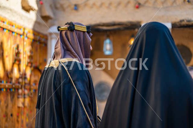 يوم بدينا 1727 م، ارتداء الزي الشعبي في ذكرى تأسيس الدولة السعودية الاولى 22 فبراير، مفهوم الفخر والاعتزاز وحب الوطن، تصوير مقرب من الخلف لزوجين عربيين خليجيين سعوديين يرتديان  الزي التقليدي للمناسبات والأعياد الوطنية، البيوت التراثية القديمة