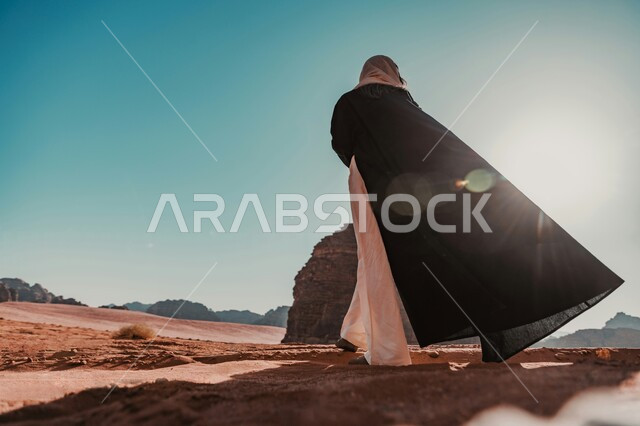 الرمال الذهبية الناعمة في البيئة الصحراوية، صورة من الخلف لرجل عربي خليجي سعودي يرتدي الزي التقليدي يقف في صحراء المملكة العربيه السعودية، الاستمتاع بالمناظر الطبيعيه في الصحاري، خلفية الطبيعه