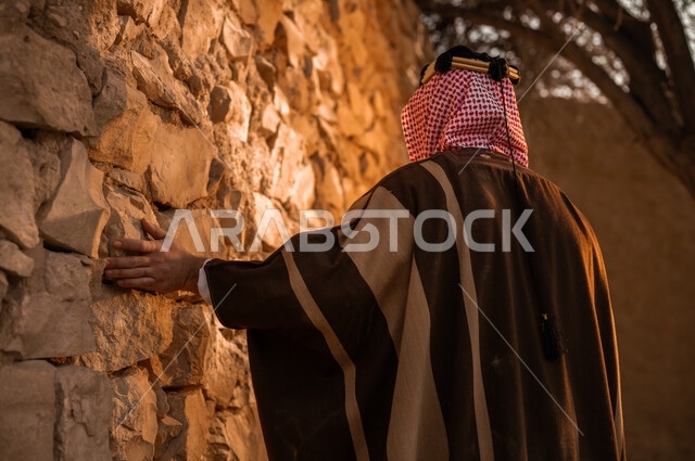 يوم بدينا 1727م, ذكرى تأسيس الدولة السعودية الأولى في 22 فبراير, الفخر بالأصالة والتراث السعودي, صورة مقربة من الخلف لرجل عربي خليجي سعودي يرتدي البشت والعقال يقف في إحدى البيوت والأحياء الطينية القديمة, ارتداء الأزياء الشعبية في الأعياد والمناسبات الوطنية