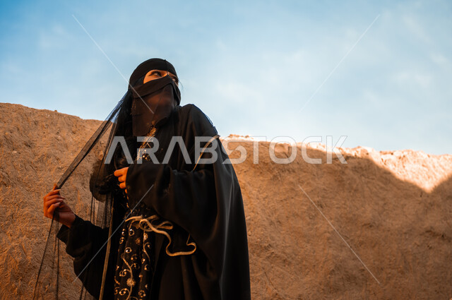 الوقوف بفخر بالهوية الوطنية, إظهار مشاعر حب الوطن والانتماء إليه, إمرأة عربية خليجية سعودية ترتدي العباءة السوداء والبرقع تنظر إلى شيء ما في إحدى البيوت التراثية القديمة, يوم بدينا 1727 م, ذكرى تأسيس الدولة السعودية الأولى في 22 فبراير، ارتداء الأزياء الشعبية