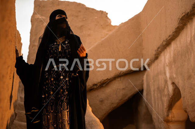 Wearing popular costumes, pride in national identity, showing feelings of love for the homeland and belonging to it, a Saudi Gulf Arab woman wearing a black abaya and burqa looking at something in one of the old heritage houses, Day of Our Day 1727 AD, the anniversary of the founding of the first Saudi state on February 22