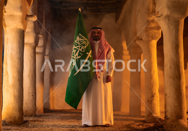 المنشآت والأعمدة التراثية القديمة, اظهار مشاعر الفخر والاعتزاز بالهوية الوطنية في ذكرى تأسيس الدولة السعودية الأولى في 22 فبراير, يوم بدينا 1727م, رجل عربي خليجي سعودي يرتدي الثوب التقليدي والشماغ يرفع العلم في العيد الوطني السعودي 23 سبتمبر, يوم العلم 11 مارس