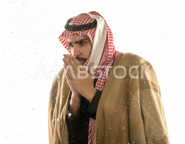 Portrait of a Saudi Gulf man with face gestures indicating feeling cold, wearing winter clothes suitable for winter, white background