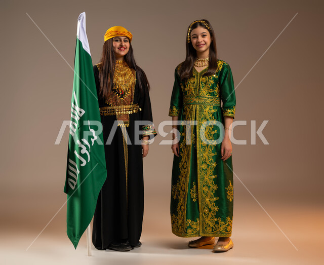 الأنوثة واللطافة والبراءة, يوم بدينا 1727 م، الوقوف بجانب علم التأسيس، ارتداء أزياء المنطقة الوسطى والجنوبية في المناسبات الوطنية، بورتريه لبنتين عربيتين خليجيتين ترتديان الزي الشعبي في ذكرى تأسيس الدولة السعودية 22 فبراير، صورة الجسم بالكامل, خلفية بيج