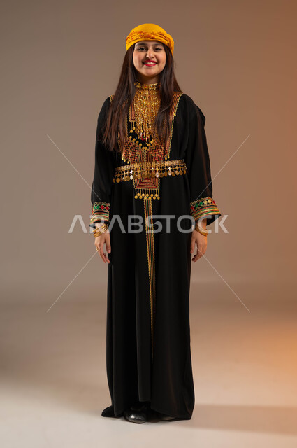 ذكرى تأسيس الدولة السعودية الأولى في 22 فبراير, ارتداء أزياء المنطقة الجنوبية في المناسبات الوطنية, بورتريه لفتاة عربية خليجية سعودية ترتدي الشيلة والسيدرة تنظر إلى الكاميرا بتعابير السرور, يوم بدينا 1727م, صورة الجسم بالطول الكامل, خلفية بيج