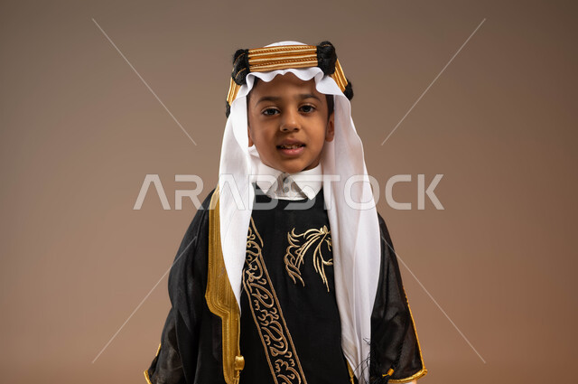 الاعتزاز بالتاريخ والتراث السعودي، يوم بدينا 1727 م، ارتداء أزياء المنطقة الوسطى في المناسبات الوطنية، ذكرى تأسيس الدولة السعودية 22 فبراير، بورتريه مقرب لولد عربي خليجي سعودي مبتسم يرتدي الغترة مع العقال الذهبي الشعبي والبشت ينظر إلى الكاميرا، خلفية بيج