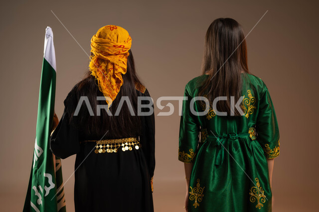 يوم بدينا 1727م, بورتريه من الخلف لفتاتين عربيتين خليجيتين سعوديتين ترتديان الزي الشعبي التقليدي في ذكرى تأسيس الدولة السعودية 22 فبراير، الوقوف باستقامة بجانب علم التاسيس بفخر, خلفية بيج