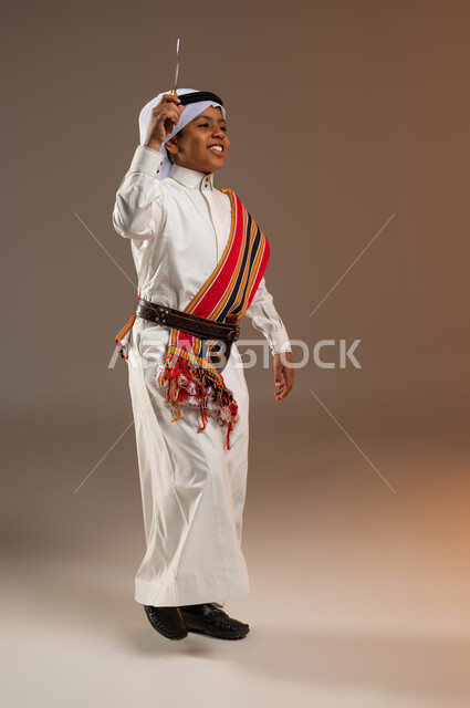 ذكرى تأسيس الدولة السعودية الأولى 22 فبراير، الرقص بالخنجر على الأهازيج والأشعار بإيماءات السعادة، ارتداء أزياء المنطقة الجنوبية في يوم بدينا 1727 م، بورتريه لولد عربي خليجي سعودي يرتدي الثوب والغترة والشال الجنوبي، صورة لكامل الجسم، خلفية بيج