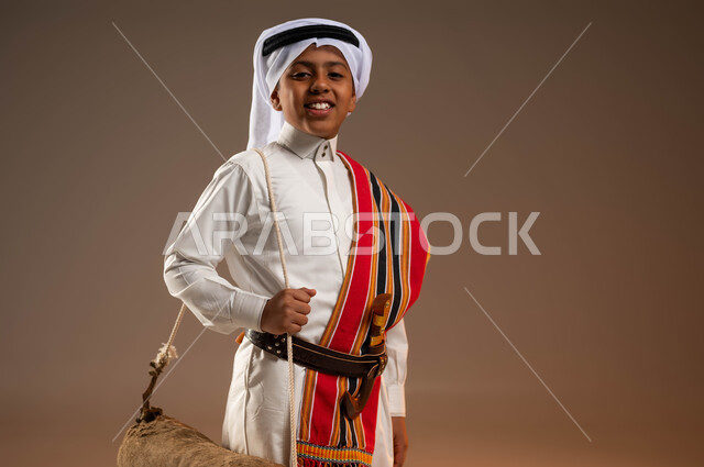 استخدام الادوات الشعبية القديمة، ارتداء أزياء المنطقة الجنوبية في يوم بدينا 1727 م، بورتريه لولد عربي خليجي سعودي يرتدي الثوب والغترة والشال الجنوبي يحمل قربة الماء للسقي ينظر إلى الكاميرا بتعابير السرور، ذكرى تأسيس الدولة السعودية الأولى 22 فبراير، خلفية بيج