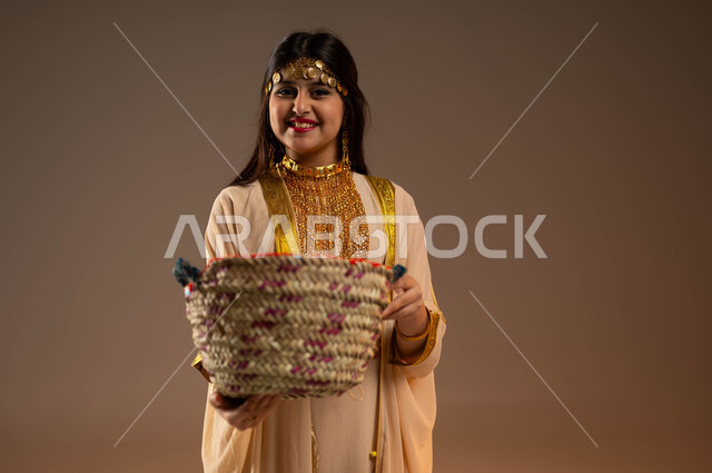 ارتداء أزياء المنطقة الشرقية، حرف ومهن يدوية قديمة، يوم بدينا 1727 م، ذكرى تأسيس الدولة السعودية 22 فبراير، بورتريه لفتاة عربية خليجية سعودية مبتسمة ترتدي النشل تحمل بيدها سلة مصنوعة من القش وتنظر إلى الكاميرا بإيماءات السرور، خلفية بيج