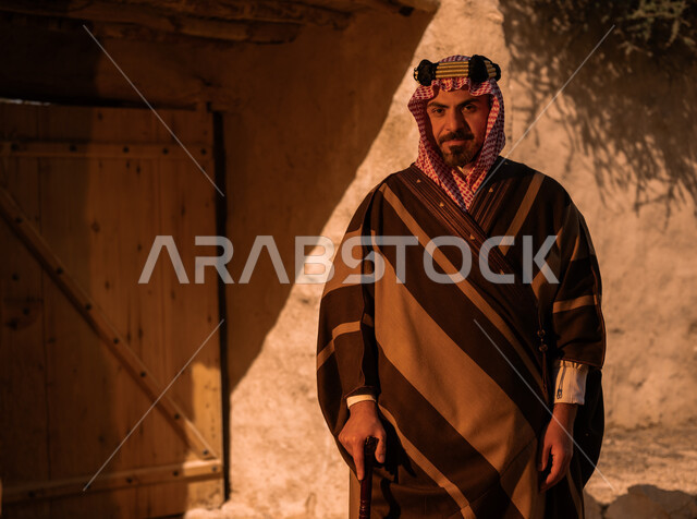 ارتداء الأزياء الشعبية التقليدية في المناسبات الوطنية، تأسيس الدولة السعودية الأولى في 22 فبراير، التجول بالأحياء والبيوت الطينية الاثرية، رجل عربي خليجي سعودي يرتدي البشت والعقال الذهبي يرتكز على عصا خشبية ينظر الى الكاميرا بفخر واعتزاز، ذكرى يوم بدينا 172 م