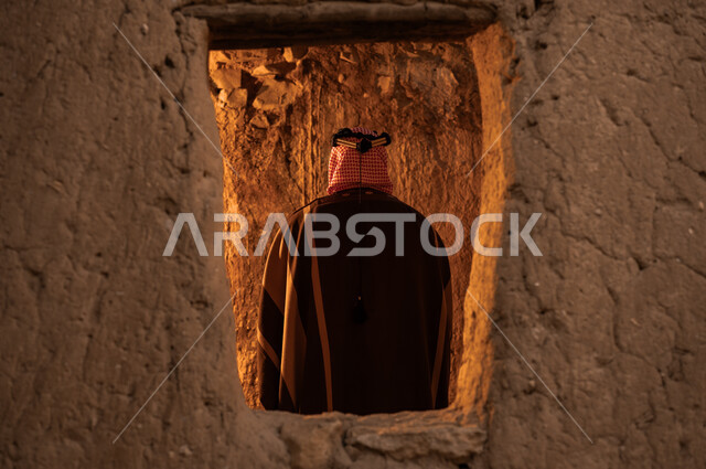 تأسيس الدولة السعودية الأولى في 22 فبراير، التجول بالأحياء والبيوت الطينية الاثرية، صورة من الخلف لرجل عربي خليجي سعودي يرتدي البشت والعقال الذهبي يتأمل التراث القديم، ذكرى يوم بدينا 172 م, ارتداء الأزياء الشعبية التقليدية في المناسبات الوطنية