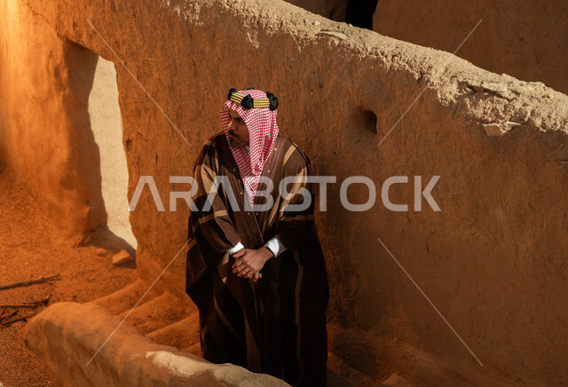  الفخر والاعتزاز بتراث الوطن، ذكرى تأسيس الدولة السعودية الأولى 22 فبراير, صورة من الأعلى لرجل عربي خليجي سعودي يرتدي البشت والعقال الذهبي يقف على درج في بيت أثري طيني قديم في السعودية, يوم بدينا 1727م، ارتداء الأزياء الشعبية في الأعياد والمناسبات الوطنية