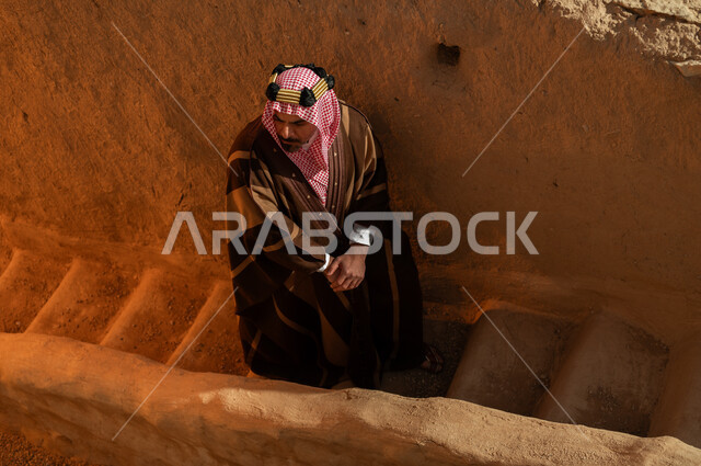 ذكرى تأسيس الدولة السعودية الأولى 22 فبراير, صورة من الأعلى لرجل عربي خليجي سعودي يرتدي البشت والعقال الذهبي يقف على درج في بيت أثري طيني قديم في السعودية, يوم بدينا 1727م، ارتداء الأزياء الشعبية في الأعياد والمناسبات الوطنية، الفخر والاعتزاز بتراث الوطن