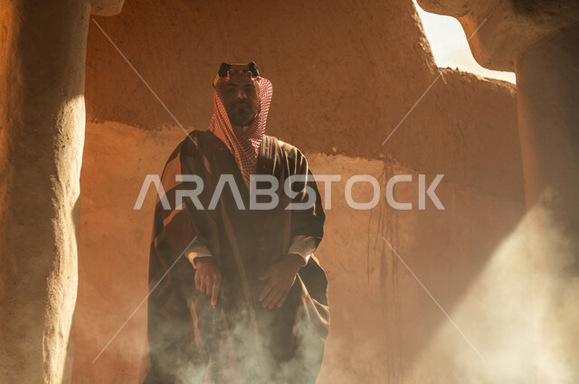 الفخر والاعتزاز بتراث الوطن، ذكرى تأسيس الدولة السعودية الأولى 22 فبراير, رجل عربي خليجي سعودي يرتدي البشت والعقال الذهبي يقف في أحد البيوت والأحياء الأثرية الطينية القديمة في السعودية, يوم بدينا 1727 م، ارتداء الأزياء الشعبية في الأعياد والمناسبات الوطنية
