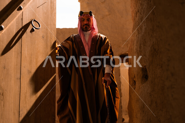 ذكرى تأسيس الدولة السعودية الأولى في 22 فبراير، الأحياء والبيوت الطينية الاثرية التاريخية، رجل عربي خليجي سعودي يرتدي البشت والعقال الذهبي يقوم بفتح باب خشبي كبير، يوم بدينا 1727 م، الاعتزاز والفخر بأصالة الوطن، ارتداء الأزياء الشعبية في المناسبات الوطنية