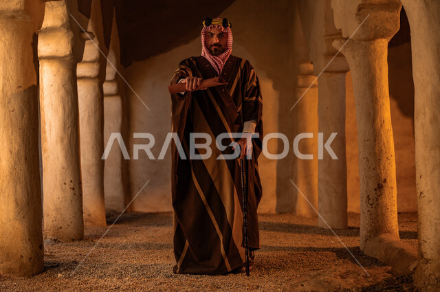 الاعتزاز والفخر بأصالة وتاريخ البلاد، ذكرى تأسيس الدولة السعودية الأولى 22 فبراير، رجل عربي خليجي سعودي يرتدي البشت والشماغ مع العقال الذهبي يمسك بيده رسائل الملك عبد العزيز الأثرية في احد البيوت الطينية، الحفاظ على الأثار والمخطوطات التاريخية، يوم بدينا 1727 م