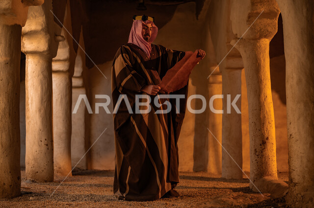 A day in the year 1727 AD, pride in the country’s authenticity and history, the anniversary of the founding of the first Saudi state, February 22, a Saudi Gulf Arab man wearing a bisht and shemagh with a golden headband reading King Abdulaziz’s archaeological letters in one of the mud houses, preserving historical antiquities and manuscripts.