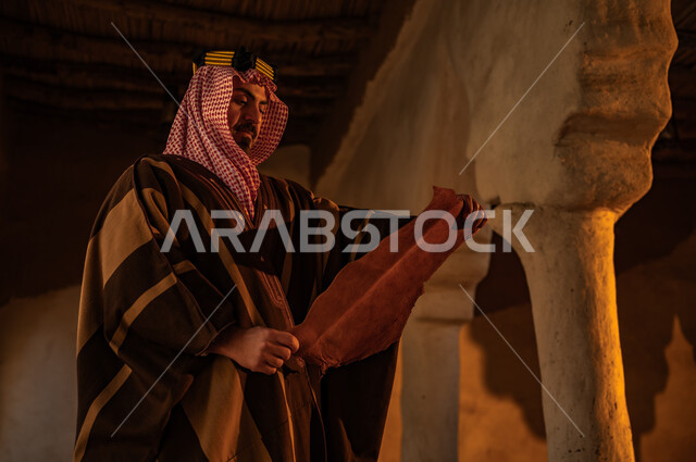 رسائل الملك عبد العزيز الأثرية، الحفاظ على الأثار والمخطوطات التاريخية، الفخر بأصالة وتاريخ البلاد، ذكرى تأسيس الدولة السعودية الأولى 22 فبراير، يوم بدينا 1727 م، صورة مقربة  لرجل عربي خليجي سعودي يرتدي الشماغ والبشت يقوم بقراءة المخطوطة في احد البيوت الطينية