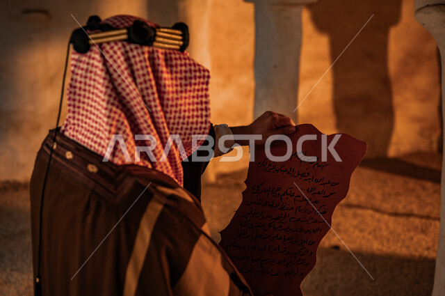 الفخر بأصالة وتاريخ البلاد، ذكرى تأسيس الدولة السعودية الأولى 22 فبراير، يوم بدينا 1727 م، الحفاظ على الأثار والمخطوطات التاريخية، البيوت التراثية الطينية القديمة، صورة مقربة من الخلف لرجل عربي خليجي سعودي يرتدي الشماغ والبشت يقوم بقراءة رسائل الملك عبد العزيز