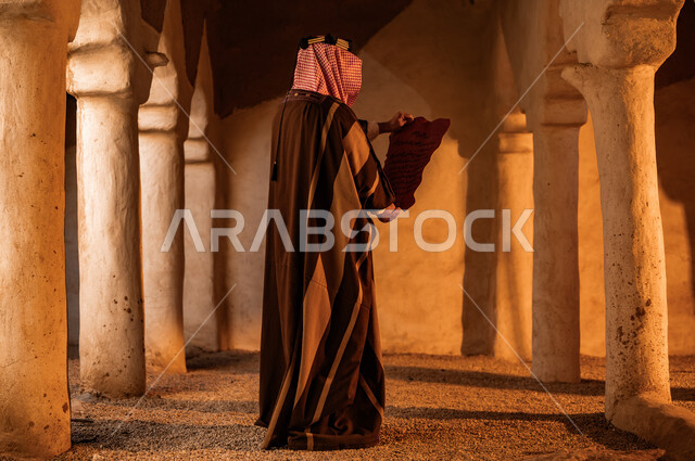 Anniversary of the founding of the first Saudi state, February 22, Day of Dina 1727 AD, ancient clay heritage columns, a picture from the back of a Saudi Gulf Arab man wearing a shemagh and bisht reading letters from King Abdulaziz, preserving historical antiquities and manuscripts, pride in the country’s authenticity and history