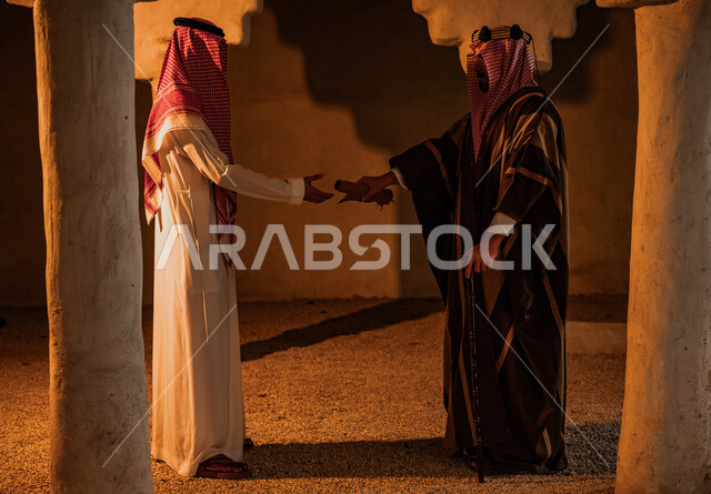 The inheritance of antiquities and manuscripts among the people of the country, the neighborhoods and the old mud heritage houses, a Saudi Gulf Arab man wearing a golden headband and a bisht giving King Abdulaziz’s letters to a young man wearing a shemagh and traditional dress, Dina Day 1727 AD, the anniversary of the founding of the first Saudi state, February 22.