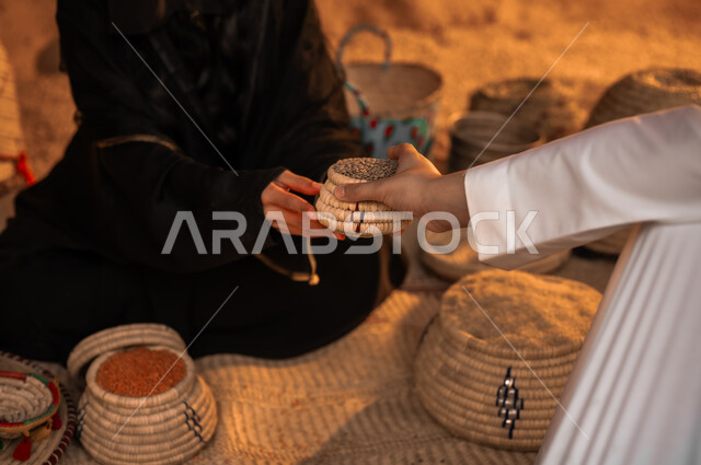  مهن وأعمال نسائية قديمة، وضع الحبوب في سلل من القش، منتجات ومحاصيل محلية وطنية سعودية، ذكرى تأسيس الدولة السعودية الأولى 22 فبراير، يوم بدينا 1727 م، صورة مقربة ليد إمرأة عربية خليجية سعودية تجلس على الحصيرة تقوم ببيع البقوليات الى الولد في حي شعبي تراثي