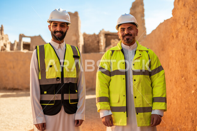 ذكرى تأسيس الدولة السعودية الأولى 22 فبراير، اكتشاف فن العمارة القديم واساسيات بناء البيوت الطينية، صورة مقربة لمهندسيين عربيين خليجيين سعوديين يرتديان السترة وخوذة الحماية ينظران الى الكاميرا يقفان باستقامة في قصر سلوى في البجيري الدرعية، يوم بدينا 1727 م