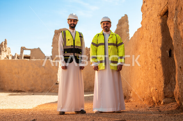 اكتشاف فن العمارة القديم واساسيات بناء البيوت الطينية، مهندسان عربيان خليجيان سعوديان يرتديان السترة وخوذة الحماية ينظران الى الكاميرا يقفان باستقامة على اطلال قصر سلوى في البجيري الدرعية، يوم بدينا 1727 م، ذكرى تأسيس الدولة السعودية الأولى 22 فبراير