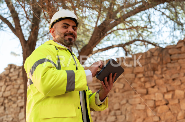 Our Day 1727 AD, learning about the art of ancient architecture, the anniversary of the founding of the first Saudi state, February 22, a close-up of a smiling Saudi Gulf Arab engineer wearing a jacket and helmet using a tablet at Salwa Palace in Al-Bujairi, Diriyah, building basics for heritage houses and palaces