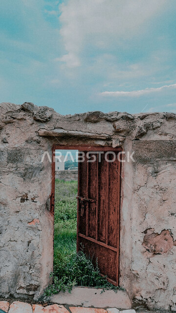 باب حديدي في إحدى القرى التراثية، الفن الهندسي المعماري للمعالم والأماكن الأثرية على الطراز القديم في قرية آل ينفع في منطقة عسير في السعودية وقت النهار، الاهتمام في زراعة النباتات و الأشجار الخضراء في القرى التراثية، معالم سياحية في المملكة العربية السعودية