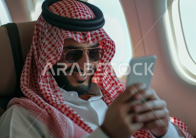 ايماءات السعادة والسرور، التواصل الاجتماعي وتصفح الانترنت، التحدث والدردشة مع الأهل والأصدقاء عبر الموبايل, صورة مقربة من الجانب لرجل عربي خليجي سعودي يرتدي الثوب التقليدي يجلس في الطائرة، رحلات جوية سياحية، استخدام الهاتف المحمول ، خطوط الطيران السعودي