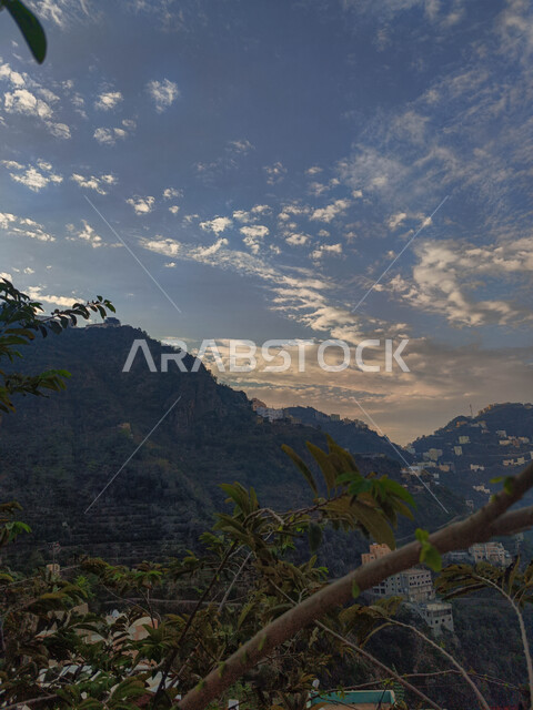 مشهد الغيوم البيضاء في السماء وقت غروب الشمس، المباني السكنية والبيوت الاثرية القديمة في جبال محافظة فيفاء في جازان، معالم وأماكن سياحية طبيعية في المملكة العربية السعودية، المدرجات الزراعية الخضراء والاشجار على القمم والمرتفعات الجبلية