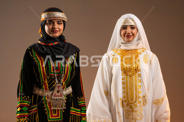 النظر الى الكاميرا بتعابير الفخر الاعتزاز، ذكرى تأسيس الدولة السعودية الأولى في 22 فبراير، يوم بدينا 1727 م، بورتريه مقرب لإمرأتين عربيتين خليجيتين سعوديتين مبتسمتين ترتديان أزياء المنطقة الوسطى والشرقية للاحتفال بالمناسبات الشعبية الوطنية، خلفية بيج