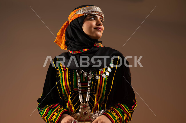 Wearing popular costumes on national occasions and holidays, commemorating the founding of the first Saudi state on February 22, standing up straight and looking at something with an expression of confidence and pride, a close-up portrait of a smiling Saudi Gulf Arab woman wearing the uniform of the central region on the Day of Dina 1727 AD, beige background.