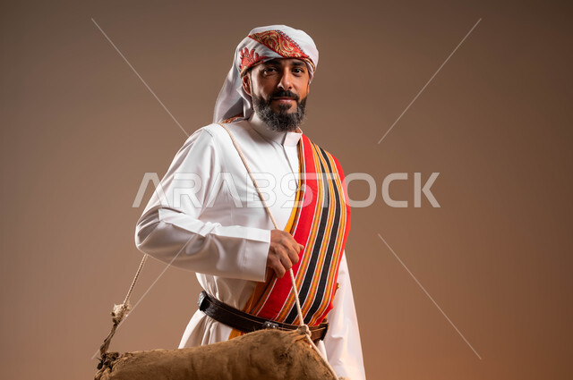 استخدام الادوات الشعبية القديمة، ارتداء أزياء المنطقة الجنوبية في يوم بدينا 1727م، بورتريه مقرب لرجل عربي خليجي سعودي يرتدي الثوب والغترة والشال الجنوبي يمشي ويحمل قربة الماء للسقي، ذكرى تأسيس الدولة السعودية الأولى 22فبراير، خلفية بيج
