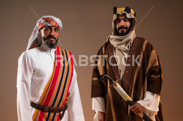 Inheritance of patriotism from ancestors, confidence and pride in the country’s achievements, close-up portrait of two Saudi Gulf Arab men wearing traditional folk costumes on national occasions, Day of Our Day 1727 AD, anniversary of the founding of the first Saudi state on February 22, beige background