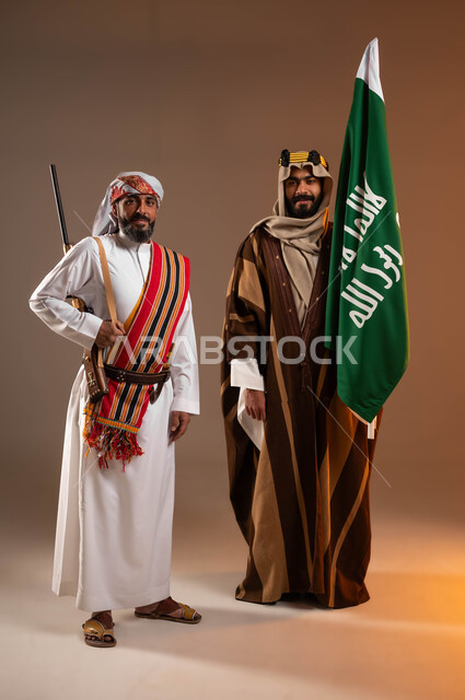 إحياء التراث الشعبي, بورتريه لرجلان عربيات خليجيان سعوديان مبتسمان يرتديان أزياء المنطقة الوسطى والجنوبية, حمل علم التأسيس والبندقية والنظر إلى الكاميرا, يوم بدينا 1727م, ذكرى تأسيس الدولة السعودية الأولى في 22 فبراير, صورة الجسم بالطول الكامل, خلفية بيج