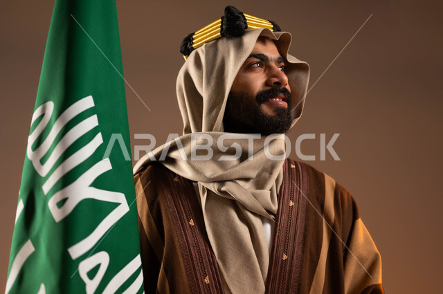 رفع علم التأسيس بتباهي، المشاركة بالاحتفالات الوطنية، الفخر والاعتزاز بالهوية العربية، يوم بدينا ٢٢فبراير،  بورتريه مقرب لرجل عربي خليجي سعودي مبتسم يرتدي العقال الذهبي والدقلة والغترة ينظر لمكان ما بانتباه، ذكرى تأسيس الدولة السعودية الأولى١٧٢٧م، خلفية بيج