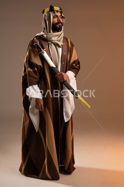 Pride in national identity, wearing popular costumes and looking at a place with gestures of pride, Day of Dina 1727 AD, portrait of a Saudi Gulf Arab young man wearing a golden iqal, daqla and ghutra carrying a sword, anniversary of the founding of the first Saudi state on February 22, beige background, full body portrait