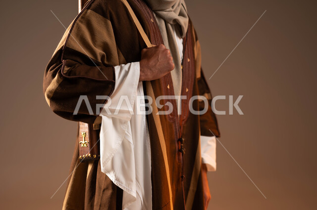 مفهوم الاصالة والعراقة عند العرب، ذكرى تأسيس الدولة الأولى 1727م، الوقوف باستقامة وشموخ، بورتريه مقرب لجسد شاب عربي خليجي سعودي يرتدي الزي الشعبي التقليدي في المناسبات الوطنية يحمل على ظهره بندقية، يوم بدينا 22 فبراير, خلفية بيج