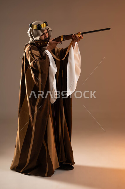 التعيين والتركيز على الهدف, براعة السعوديين في الصيد, ذكرى تأسيس الدولة الأولى 1727م, استخدام البندقية لقنص الحيوانات البرية, بورتريه من الجانب لشاب عربي خليجي سعودي يرتدي الدقلة والغترة والعقال الذهبي، يوم بدينا 22 فبراير, صورة لكامل الجسم، خلفية بيج