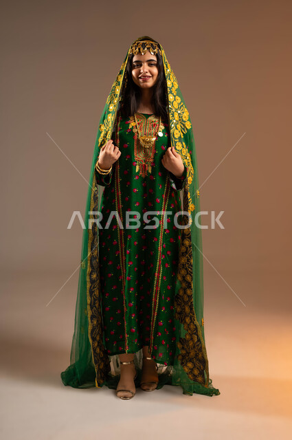 الاهتمام بالمظهر الخارجي، إيماءات السعادة والفرح، مفهوم التأنق والتجمل، بورتريه لإمرأة عربية خليجية سعودية ترتدي الشيلة والهامة والبشت، ارتداء أزياء المنطقة الوسطى، ذكرى تأسيس الدولة السعودية الأولى٢٢ فبراير، يوم بدينا١٧٢٧م، صورة لكامل الجسم، خلفية بيج