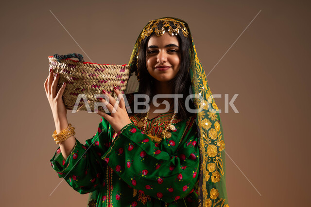 النظر إلى الكاميرا إيماءات السعادة بذكرى تأسيس الدولة السعودية الاولى ٢٢ فبراير، حرف وأعمال شعبية تقليدية، مشغولات يدوية نسائية، بورتريه مقرب لشابة عربية خليجية سعودية ترتدي الشيلة والهامة والبشت تحمل سلة مصنوعة من القش، الاحتفال بيوم بدينا ١٧٢٧م، خلفية بيج