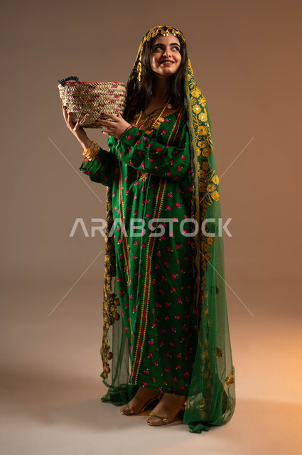 مشغولات يدوية نسائية، ذكرى تأسيس الدولة السعودية الاولى ٢٢ فبراير، أعمال وحرف شعبية تقليدية، بورتريه لشابة عربية خليجية سعودية ترتدي الشيلة والهامة والبشت تحمل سلة مصنوعة من القش تنظر بانتباه إلى مكان ما، الاحتفال بيوم بدينا ١٧٢٧م، صورة لكامل الجسم، خلفية بيج